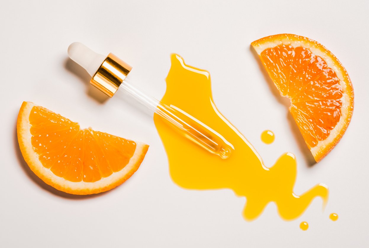 Pipette mit auslaufender gelber Flüssigkeit und zwei Scheiben Orangen daneben